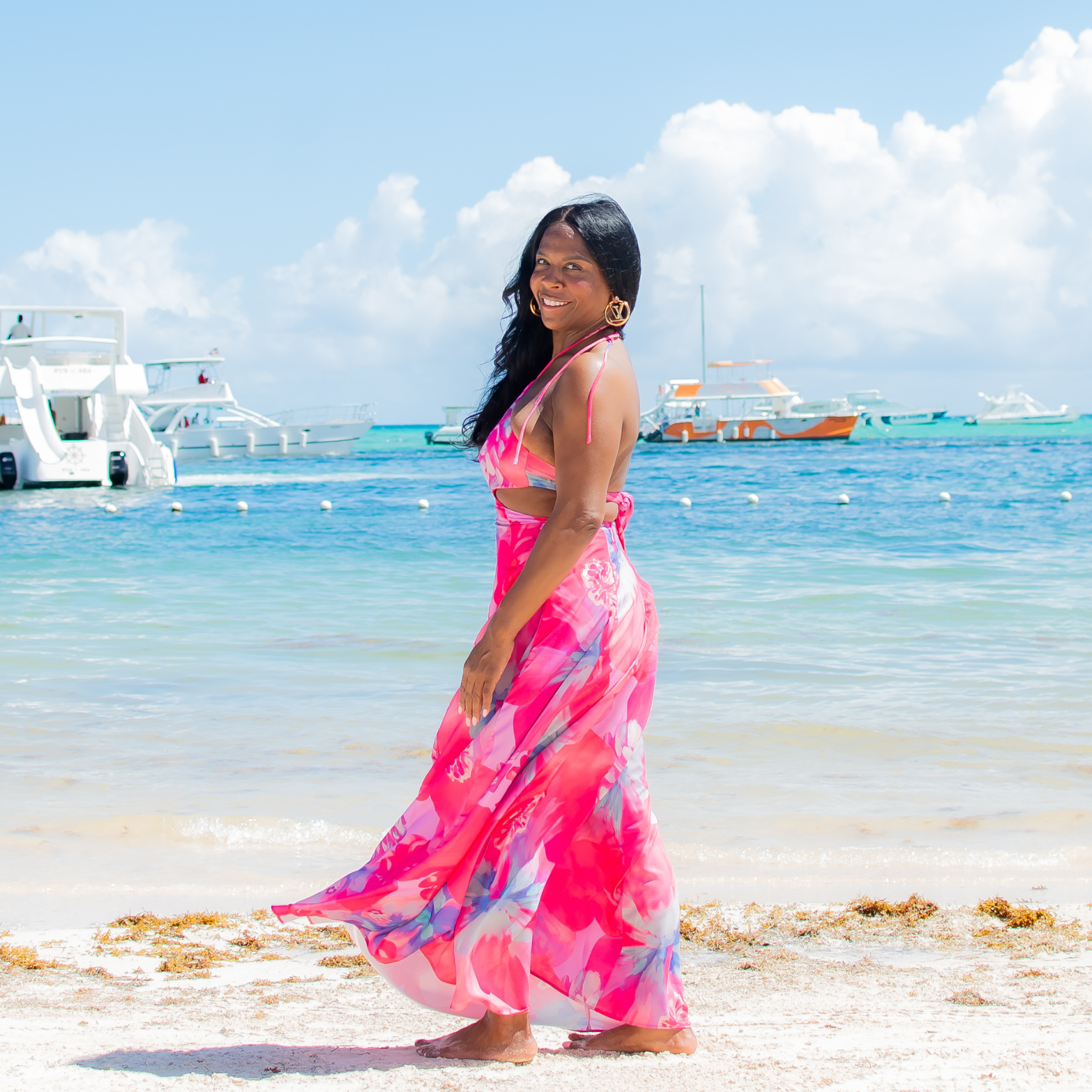 Woman in a pink dress standing on a beach with clear blue water and sky.