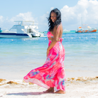 Woman in a pink dress standing on a beach with boats in the background