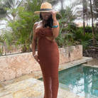 Woman in a brown dress and hat by a pool with palm trees in the background