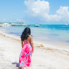 Woman in a pink dress standing on a beach with boats in the background